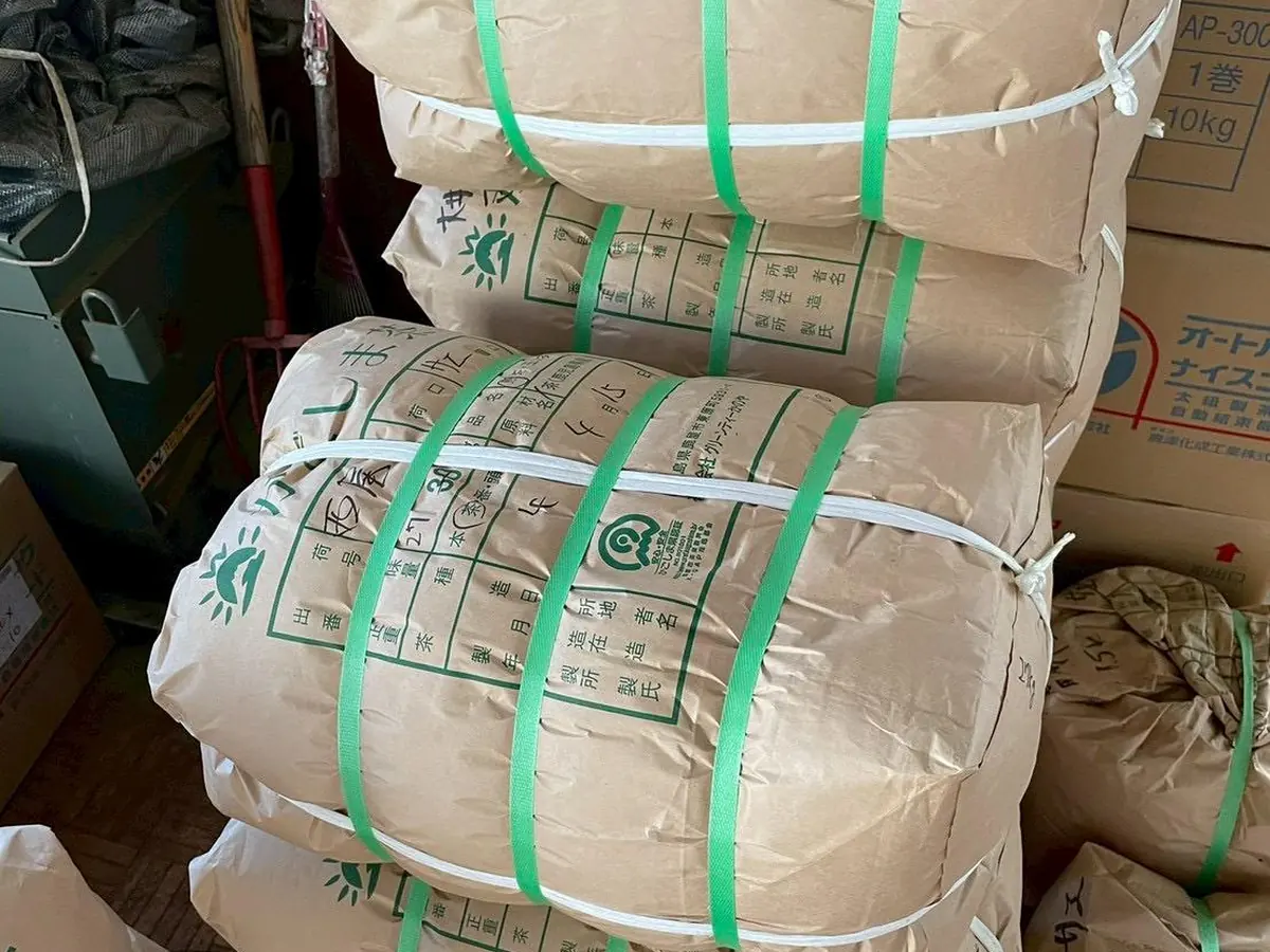 Paper-wrapped bales of processed tea banded and stacked in a Japanese tea warehouse, each carrying its lot markings