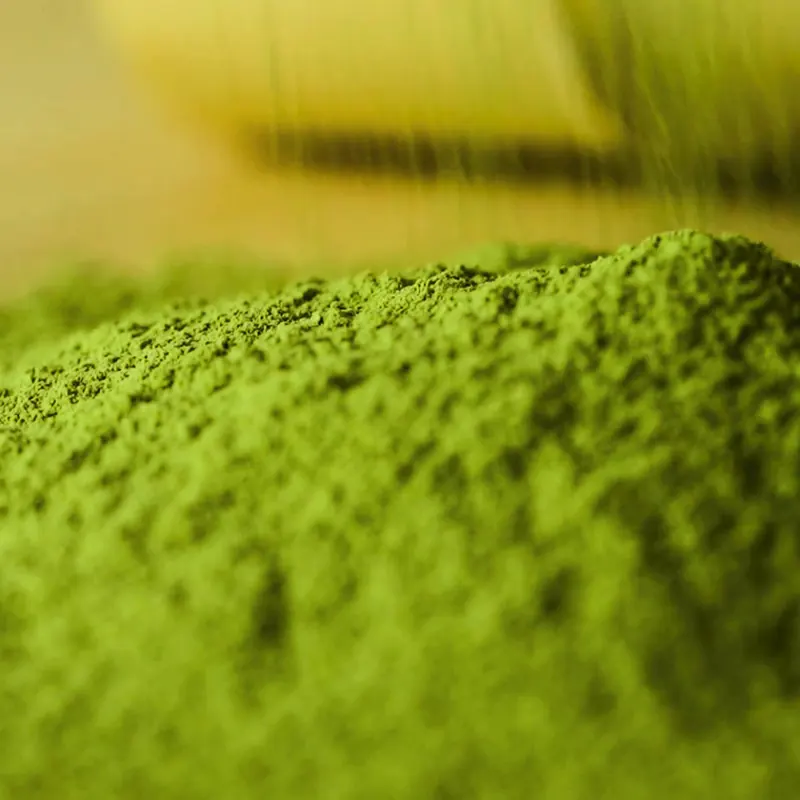 Stone-milled matcha powder heaped beside a bamboo whisk